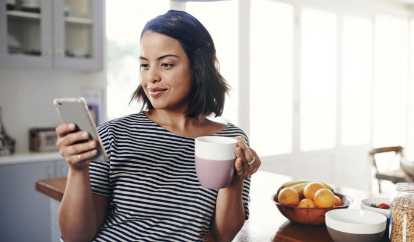 Person on phone with coffee in kitchen