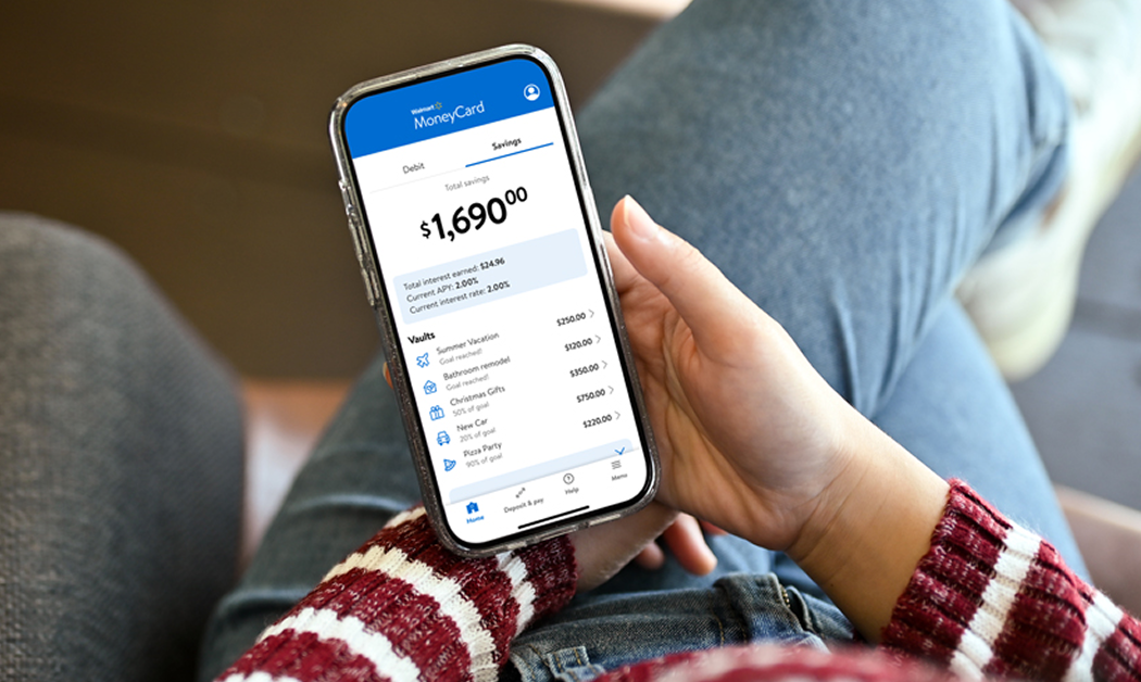 Woman looking down at a smartphone showing the Walmart MoneyCard app looking at her savings account balance of $1,690.00.